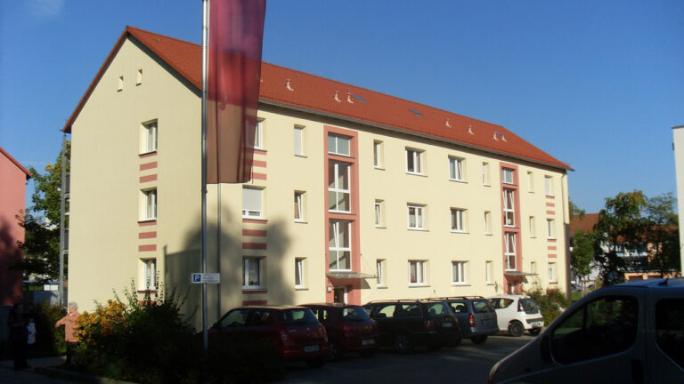 Ein Bild nach der Sanierung eines Hauses in der Gerhart-Hauptmann-Straße 1-11. Es präsentiert sich in modernem Stil, mit einem frischen Pastellgelb und dezenten orangefarbenen Fensterakzenten.
