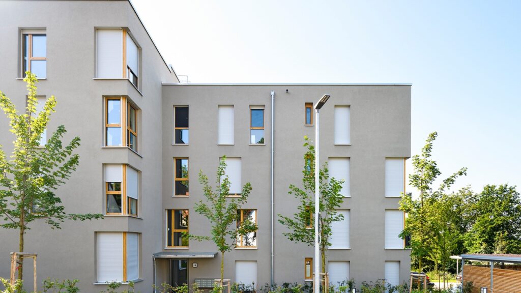 Nach der Renovierung: Gebäude 38 in der Mayer-Franken-Straße. Ein grauer Beigeton dominiert die Fassade, während die Fenster mit lebhaftem Gelb akzentuiert sind. Alle Fenster sind in länglicher Form gestaltet.